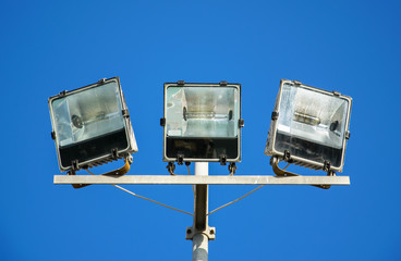  Close Up of a modern white metallic street lamp post with three lanterns against clear blue sky.