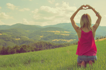 Girl making a heart-shape with her hands outdoors.