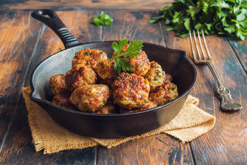 Homemade roasted beef meatballs in cast-iron pan on wooden table in kitchen.