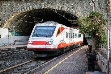 Fototapeta premium White passenger train driving out from tunnel near Vernazza town, Cinque Terre, Italy