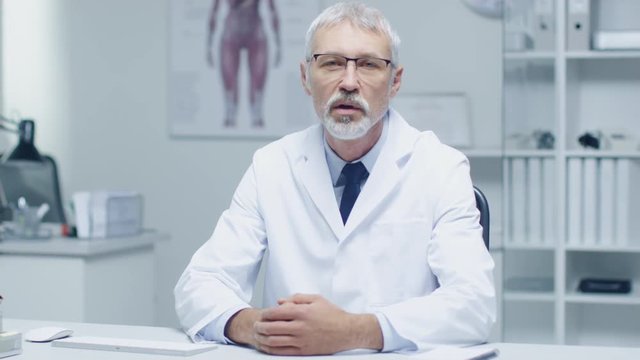 Experienced Gray Haired Senior Medical Practitioner Talking Into Camera. Portrait Shot in Modern and Light Office.  Shot on RED Cinema Camera in 4K (UHD). 