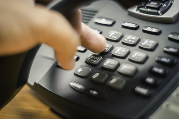 businessman dialing voip phone in the office, keyboard and monitor detail in the background with vintage color tone effect