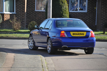 A blue British sports saloon braking at a T Junction on a housing estate in the UK.

