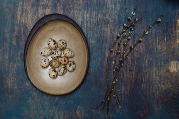 Simple still life with hand-crafted ceramic plate quail eggs and pussy willow on distressed wooden table.