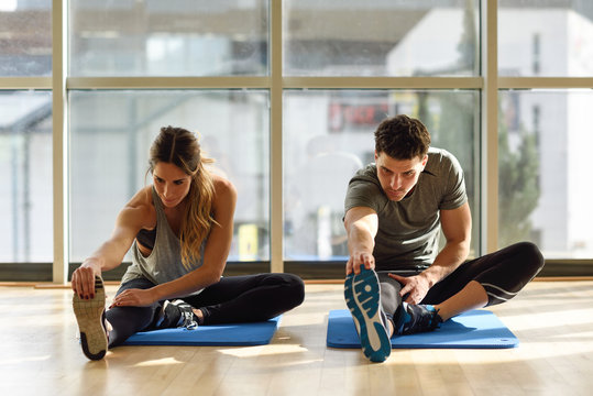 Fototapeta Two people streching their legs in gym.