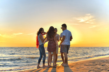 group of happy young people dancing at the beach on beautiful summer sunset