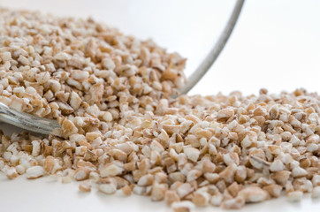 Pile of the uncooked raw cut wheat near glass bowl. Healthy lifestyle concept. Closeup macro shot.