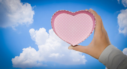 Right hand holds heart with blue sky background 
