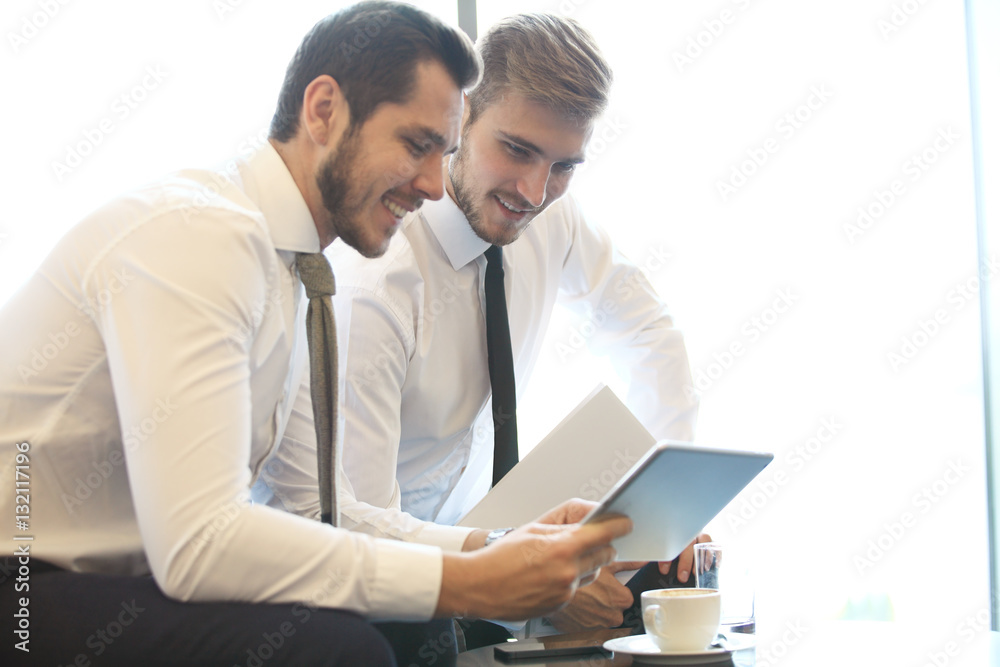 Wall mural image of two young businessmen using touchpad at meeting.