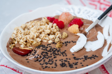 Chocolate smoothie bowl of oatmeal, sesame seeds and raspberries for breakfast. Love for a healthy raw food concept.