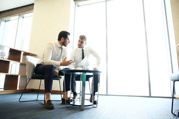 Image of two young businessmen using touchpad at meeting.