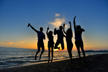 group of happy young people dancing at the beach on beautiful summer sunset