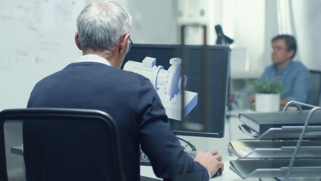 Backview of Senior Engineer Working with 3D Model on His Personal Computer. Also His Assistant Came in the Office and Took Place at His Desk.  Shot on RED Cinema Camera in 4K (UHD). 