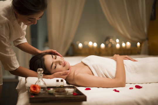 Young woman receiving facial massage from masseuse in spa