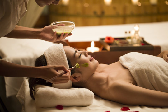 Young woman receiving facial treatment from masseuse in spa