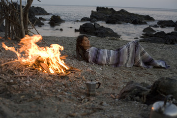 femme qui campe couchée sur la plage au coin du feu