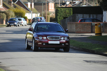 A Maroon estate car driving down a suburban street in the UK