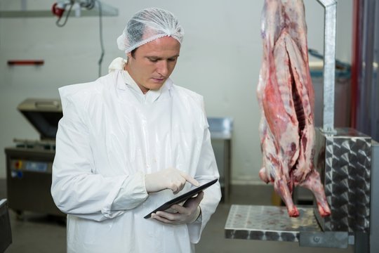 Male butcher maintaining records on digital tablet