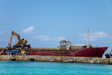 Excavator on top of a docked ship in George Town harbor, Grand Cayman, offloads dirt into a dump truck