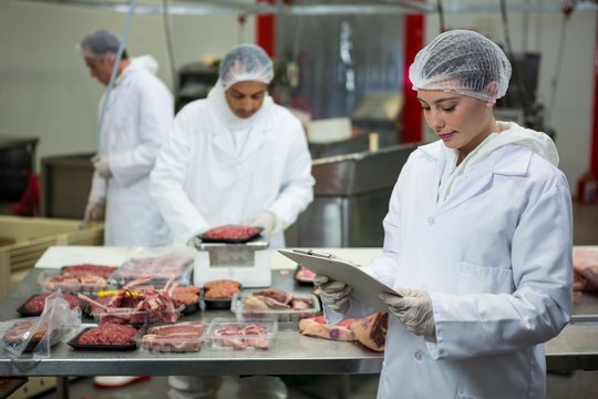 Female butcher maintaining records on clipboard