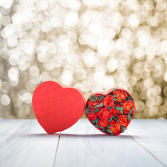 Heart shape box with red roses inside on white wood table top with gold bokeh