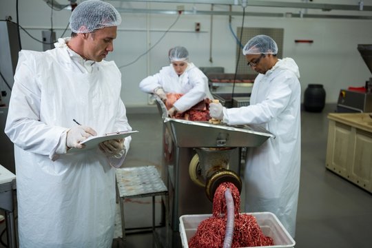 Butchers placing meat in mincing machine