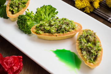 Tartlets stuffed with minced meat  broccoli and tuna. Wooden background