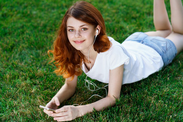 Fototapeta premium beautiful young woman in a light t-shirt, relaxing on the grass in a park, trees, nature