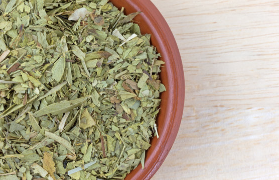 Bowl filled with cut and sifted senna leaf top close view atop a wood table.