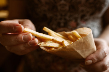 French fries eating close-up. Unrecognizable woman taking fried potato from paper pack. Junk fast...