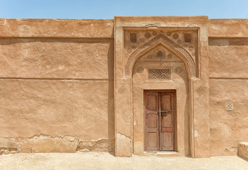 A traditional arched doorway with gypsum carvings and a carved door stands in bright sunlight in a...