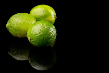 Three green limes against a black background with reflection