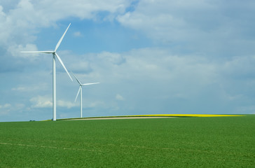 Rural landscape in France with blue sky and green field with spinning wind power stations producing environmentally friendly electric energy.