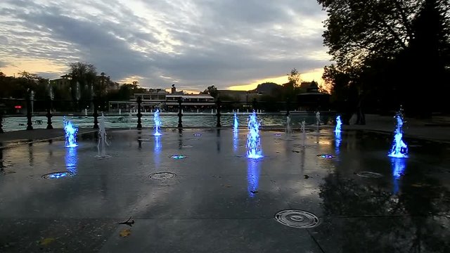 Colorfully lit fountain in a park at dusk