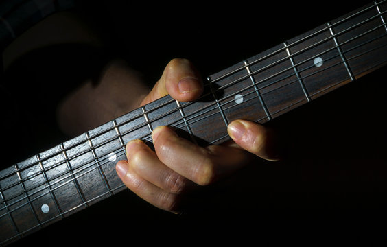 A man's hand playing an electric guitar in the dark