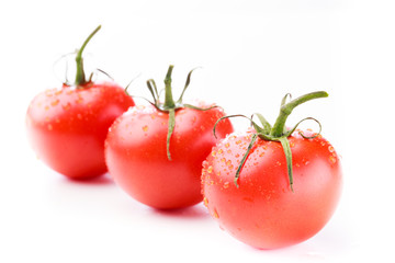 Three ripe tomatoes with green stems and water droplets in a diagonal line on a white background