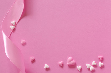 Schleifenband mit Zuckerherzen auf rosa Untergrund