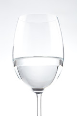 Close up of isolated wine glass partially full of water with a thin stem on a white background