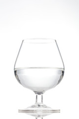 Short stem wine glass half full of water on a white background with a reflection
