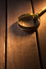 Magnifying glass with shadow under beam of light on wooden background