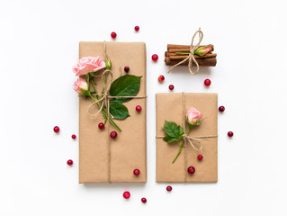 Gift box and envelope in eco paper on white background. Presents decorated with roses and berries. Holiday concept, top view, flat lay
