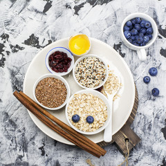 Ingredients for homemade oat cereal biscuits with flax seed, sesame seeds, dried cranberries, blueberries on a marble background. Top view. The concept of health food