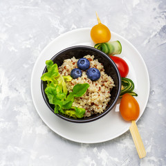 Healthy breakfast snack. Quinoa bowl with fresh vegetables, berries and herbs on a marble background in portioned bowls    . Top view