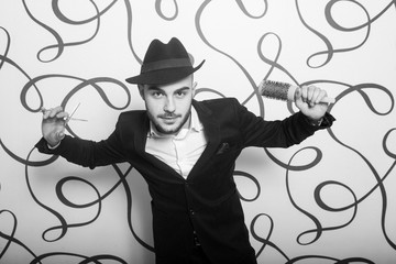 Ragazzo parrucchiere con forbici e spazzola  in mano che si diverte a posare in studio 