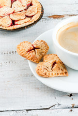 Idea for the celebration of Valentine's Day: cherry pie with the decor of the test in the shape of a heart, one bite of cake with a cherry in the form of hearts and a cup of coffee, close view