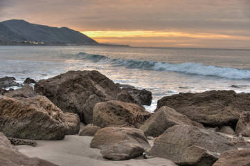 Ocean boulders covered in barnacles on California beach at dawn.