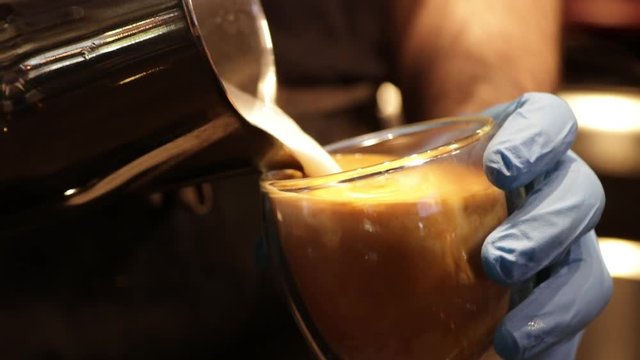 Puring hot milk with foam into a glass with espresso