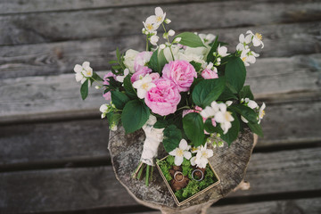 Beautiful bouquet of jasmine and pink garden roses and a box with moss and wedding rings on old wooden stump