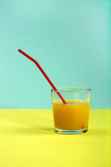 Стакан сока с соломкой (трубочкой) на цветном фоне
