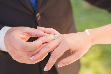 Closeup of a groom putting a gold wedding ring onto the bride's finger